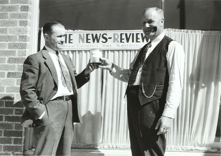 Photograph depicts Frank B. Robinson handing Mr. Henry Banks a can of 'rattlesnake meat' out front of the building of the publication, The News Review.